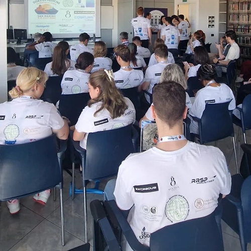 Gruppo di partecipanti con magliette bianche personalizzate con i loghi degli sponsor davanti a un'autopompa dei vigili del fuoco